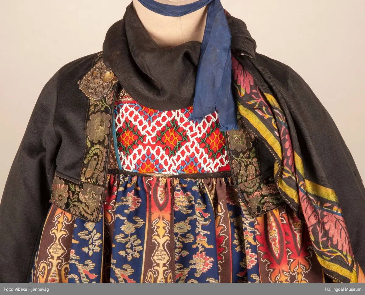 Kone fra Nedre Hallingdal i hallingbunad.  Kona står utstilt i den faste bunadutstillingen på Hallingdal Museum, Nesbyen.  Hallingbunaden består av mange draktdeler; trøye HFN 03608, Forkle HFN 02016, stakk, liv, lue, silketørkle rundt lua, silketørkle rundt halsen HFN 11158, bringduk og skjorte.