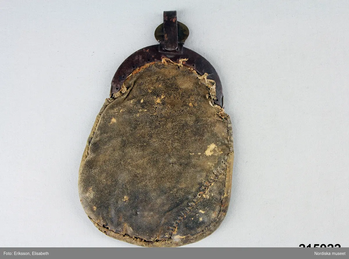 "Kjolsäck, framsida röd vadmal, applikation i olikfärgad vadmal, tennbroderier; bygel, ornerad mässing; hake mässing, märkt UDP 1814; baksida skinn."
/enligt intendent Inga Wintzells anteckningar