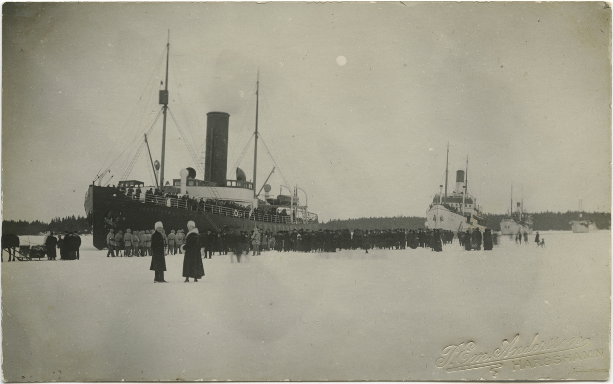 Passagerare på isen framför Isbrytaren II (sedermera Sankt Erik) under Ålandsexpeditionen, Hargshamn 24 februari 1918. Isbrytaren ledde konvojen som syns i bakgrunden. Från vänster Isbrytaren II, Svea-rederiets Heimdall (b. 1915, reg nr 5715), Vineta (b. 1913, reg nr 5403) och J.L. Runeberg (b. 1876, reg nr 1541). Vineta skulle två dagar senare skruvas ned av ismassor och förlisa vid Mäntyluoto.
