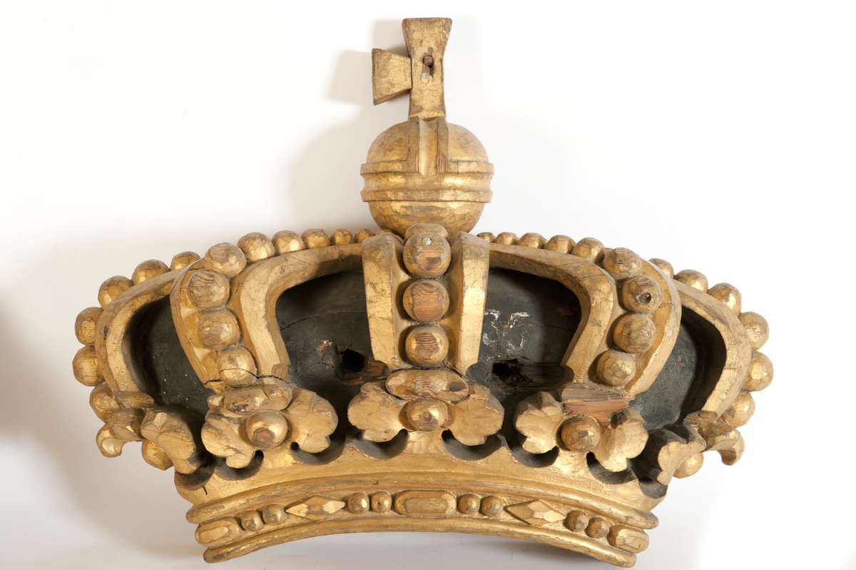 Akterspegelornament tillhörande linjeskeppet KARL XIV JOHAN, bestående av sköld, krona med äpple. Ej konserverad
a) Sköld cirkelrund med Karl XIV Johans namnschiffer, förgylld på blå refflad botten. Kantlisten förgylld. Märkt: ?50? på vidhäftad plåt. Diameter max 1085 mm Diameter min. 1050 mm
b) krona, kunglig förgylld med svart botten, två bulthål. Bredd: 850 mm. Höjd: 390 mm
c) Äpple med kors, förgylld, deffekt. Höjd med fästlapp: 350 mm. Diameter: 160 mm.