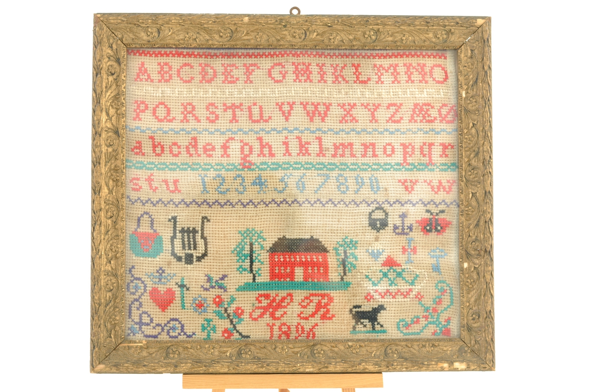 Navneduk fra 1896. Korssting på stramei. Navneduken er rammet inn med glass og ramme på et senere tidspunkt.