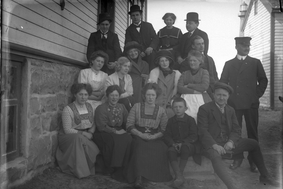 Gruppebilde av menn og kvinner på en trapp, med Andenes fyr i bakgrunnen.