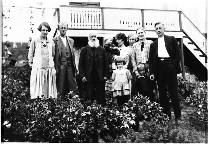 Gruppebilde av Lars Johnsen med familie, tatt i hagen foran et hus.