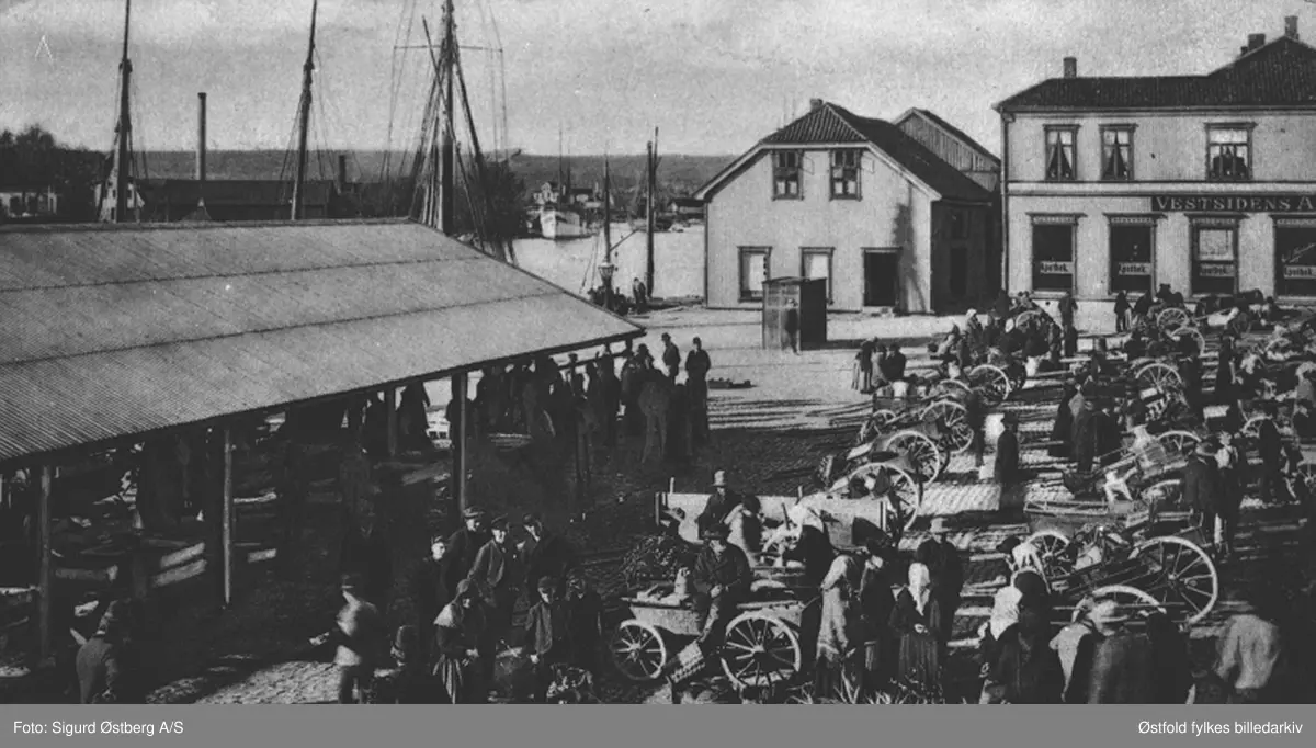Fisketorvet i Fredrikstad, 1900. Postkort.
Fiskebrygga og torvet i Fredriksstad, i front Haanshus-gårdene som brant i 1908, til venstre sees skuret hvor fiskebasarene  lå. 

Motivet stammer fra en mappe med seks bybilder, utgitt av Sigurd Østberg papirforretning i 1900.