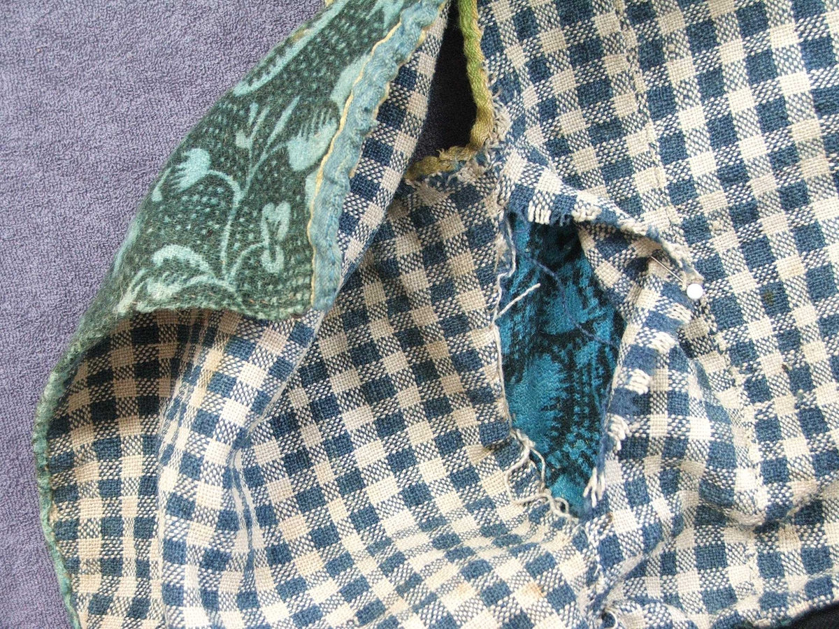 Mønster på liv : Mørk grøne blomar og blad på lys grøn og mørk grøn/lysgrøn-rutet botn. Noko som liknar drueklasar, fleire typar blad og blomar.