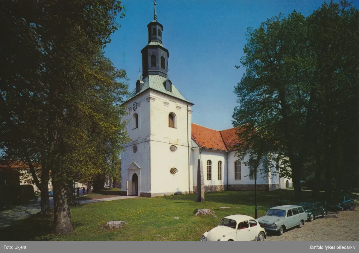 Østre Fredrikstad kirke, i Gamlebyen, Fredrikstad ca. 1965-70. 
Flere biler parkert. Volkswagen boble, Ford Cortina stasjonsvogn . Postkort. Tittel på postkortets bakside er feil.