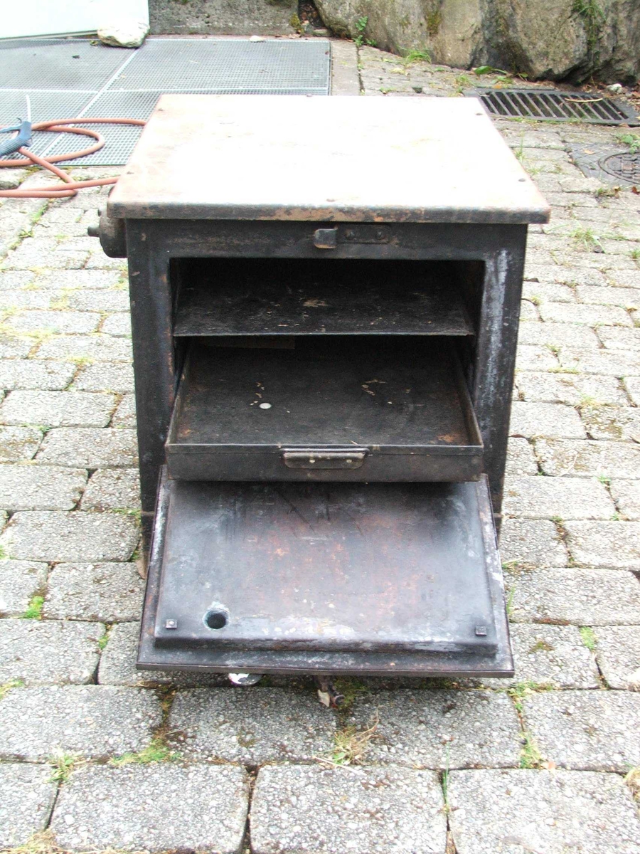 Elektrisk steikjeomn. Dør på eine kortsida med lukkemekanisme øvst. Tjukke veggar. Inni er det to lause steikjeplater. Det er spor til å setje plater på på veggane. Ei plate har kant, den andre ikkje. Øvst på eine langsida er det fire brytarar. Ledning kjem ut på kortsida bak.