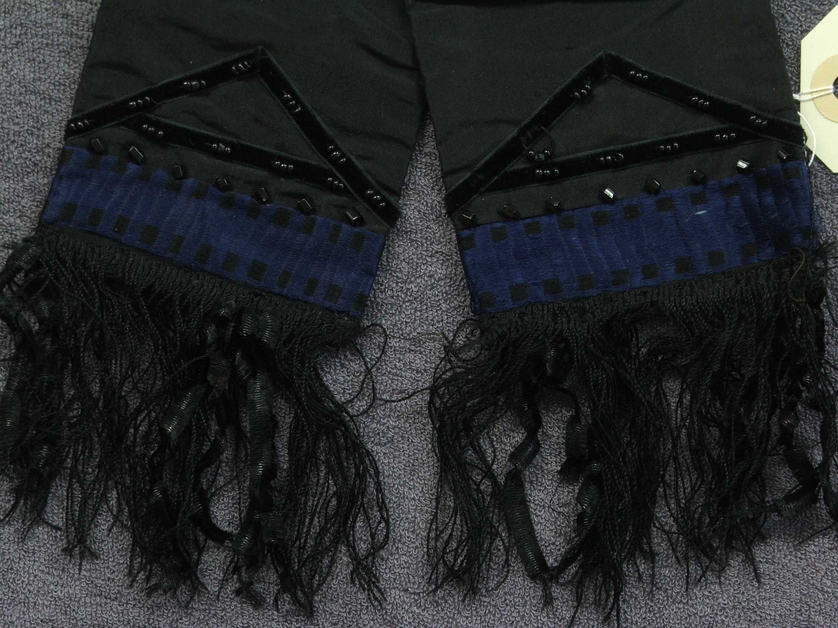 Svart sløyfe, pynt til bluse eller hovudplagg. Silkefrynser, fløyelsband, glasperler sydd på. Fôra.