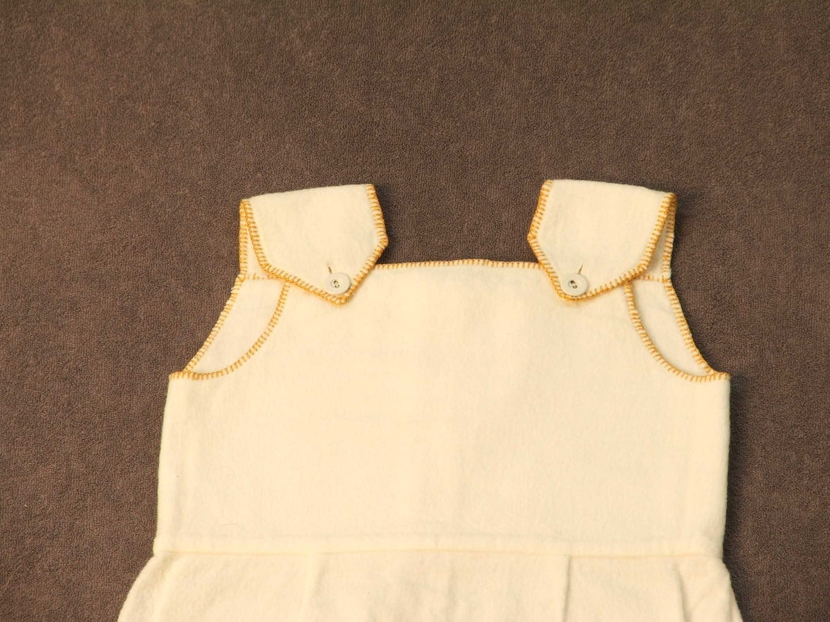 Den øvre delen er kanta med gule sting. Lerretsknappar; ein på kvart berestykke og for loddrett lukking 4 i øvre delen. Nedanfor knappane eitt stoffstykke som i kvar av dei to loddrette, innbretta sidene har 2 raude og ei blå stripe.