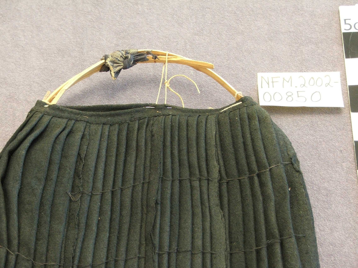 På vranga er det sydd kanting med 7,5 cm.bomullsstoff . Stoffet har loddrette striper i brunt, grønt, svart, raudt, blått.På ein del nedst: svart fløyelskant.