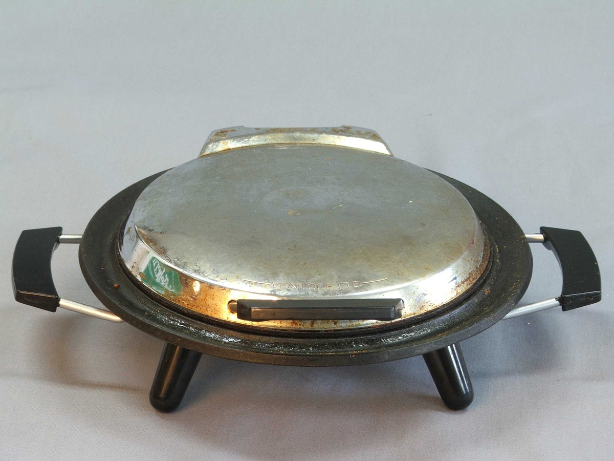 Eit vaffeljarn i original øsjke, isopor i øskja som jarnet står på. Det er ikkje ledning. Jarnet: Rund form. Loket opnast med handtak midt framme. Loket er hengsla fast til underdelen. Loket kan stå oppe av seg sjølv. Utsida av jarnet: oppå og under er det blankt metall, svart handtak på lok og to på kvar side av understellet. Inni er jarne svart, støypejarn? Vaffelhjarte-formar inni jarnet både på lok og botn = fem små hjarte som dannar ein sirkel. Fire svarte bein på undersida som jarnet står på.
Øskja er grøn med ein gul vaffel på oppsida og eit kvitt hjarte på sida. Øskja kan du opne framme. Den er kvit inni.