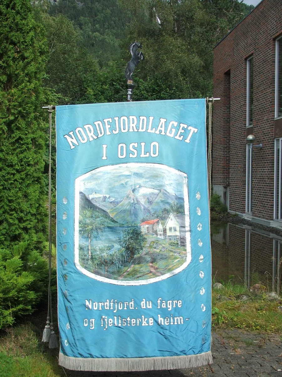 Gardstun med fjord, fjell og bre i bakgrunnen på framsida. På baksida skal det vere Holvikejekta som er måla i ein enkel strek. Tekst på framsida er "Nordfjordlaget i Oslo" over måleriet. Under "Nordfjord, du fagre og fjellsterke heim". 10 blader i rad på kvar side av motivet. 