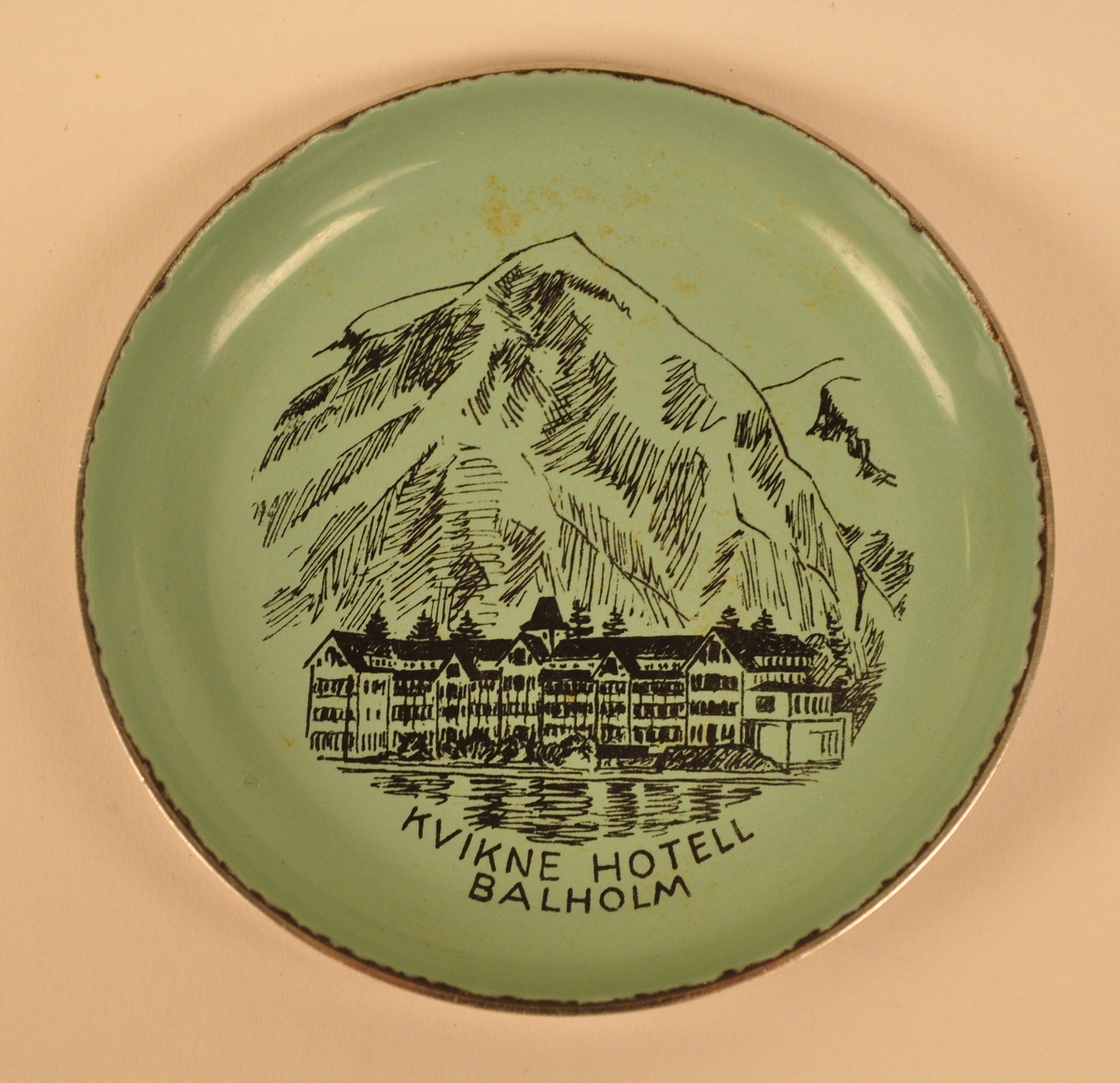 Dekoren er ei grafisk framstilling av eit stort hotellbygg i sveitserstil med eit høgt fjell i bakgrunnen og sjø i framgrunnen.