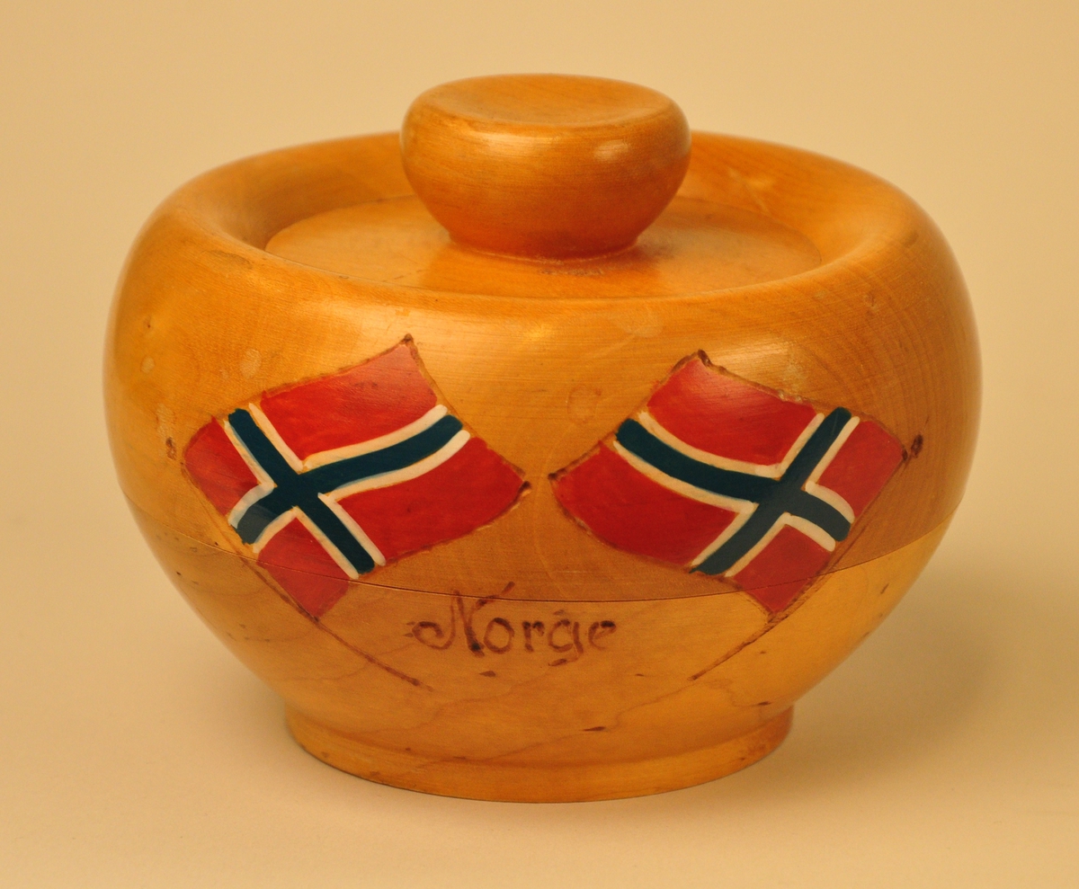 Dreia trebolle med to norske flagg og påskrift. Bollen har ein rett, liten kant å stå på før den rundar utover. Øverst rundar den innover og ned mot midten der  det er eit flatt lok med ein kraftig knott. Bollen er laga av to ulike emne som er limte oppå kvarandre.