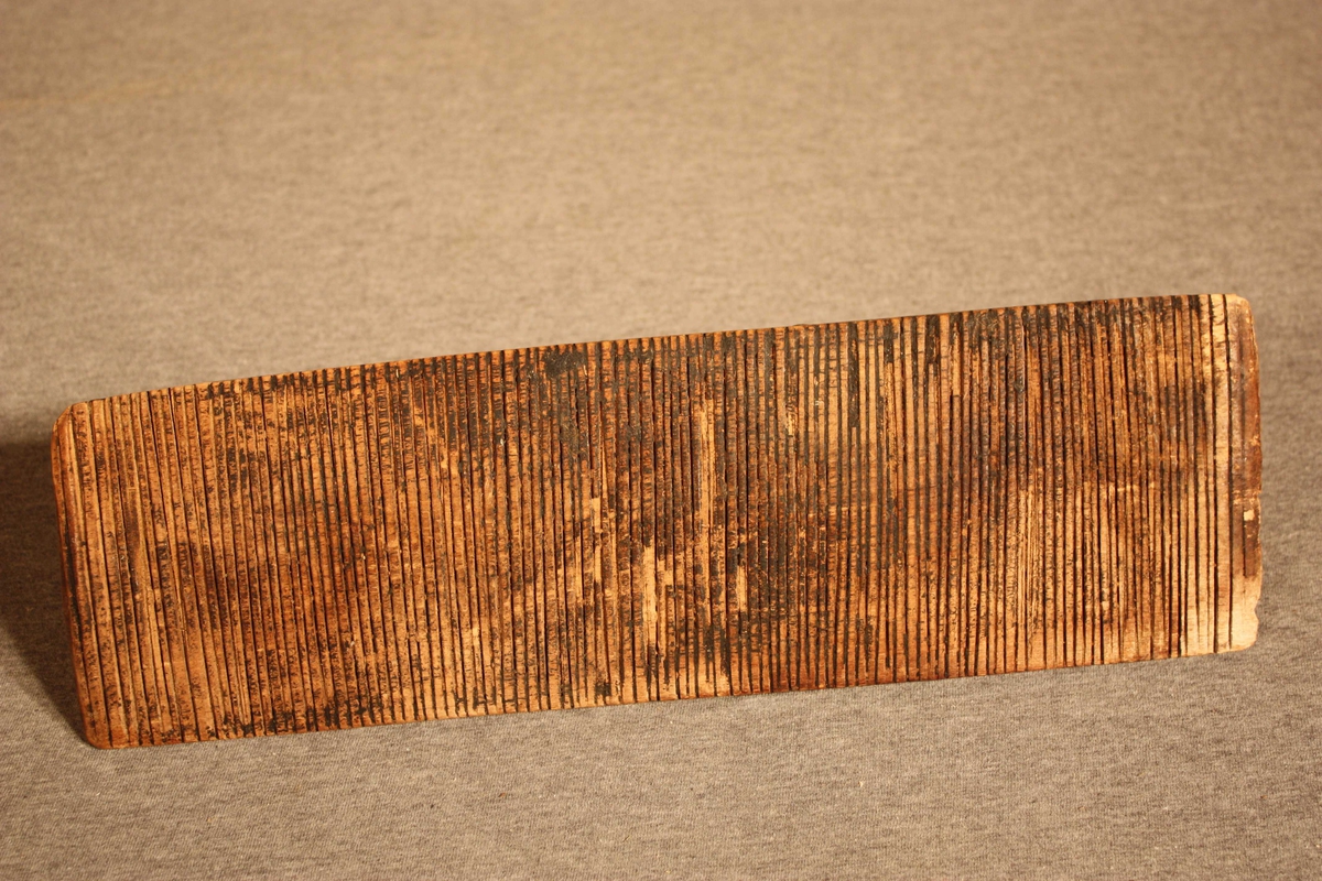 Form: rektangulær fjøl med rifla underside og handtak på oversida
