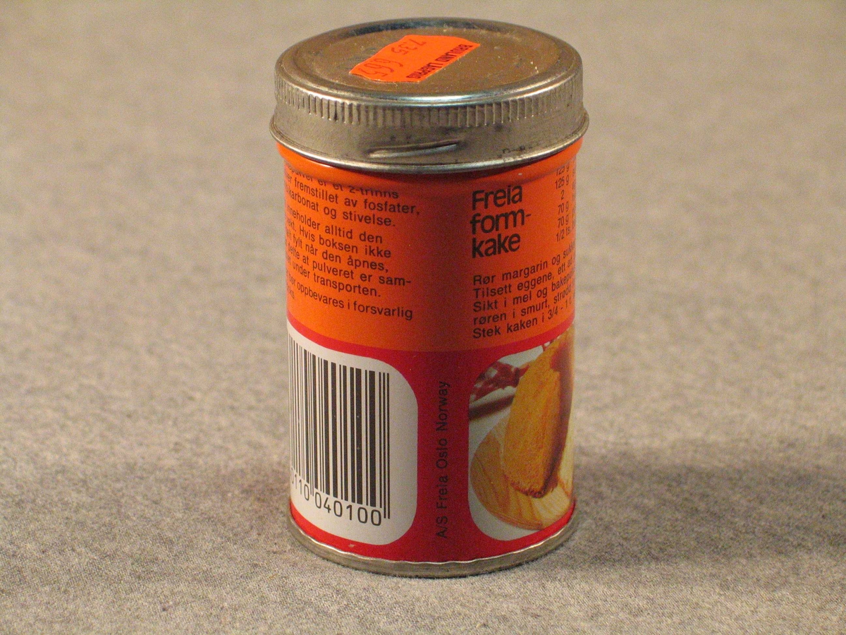 Rett blekkboks med skrulôk. Kring halvfull med bakepulver.
På lôket er orange prislapp frå Bruland Lågpris "7,35  6,65". Truleg betyr det  "vanleg pris" og "vår pris". det er strekkode på boksen, men butikken har truleg ikkje hatt avlesingsutstyr