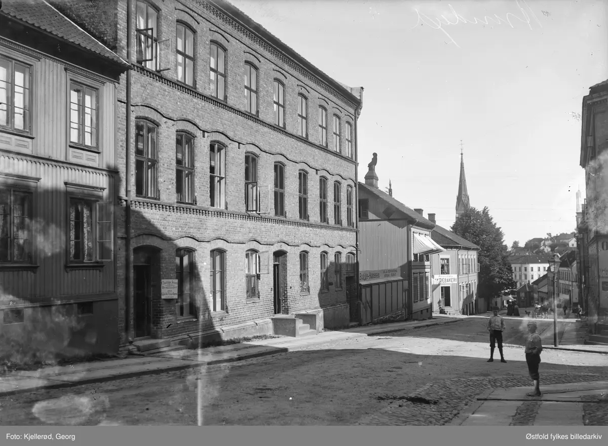 Vestregate, Arendal sett ned mot Malmbryggen/Sanden med Trefoldighetskirken i bakgrunnen.

Tekst på skilt fra venstre: 
Chatrine Jensen Bestillinger paa kjød- og fiskefarse modtages. Bugges kul og vedforretning. Østregade? Telefon 57. Arendals Aktiemeieri.