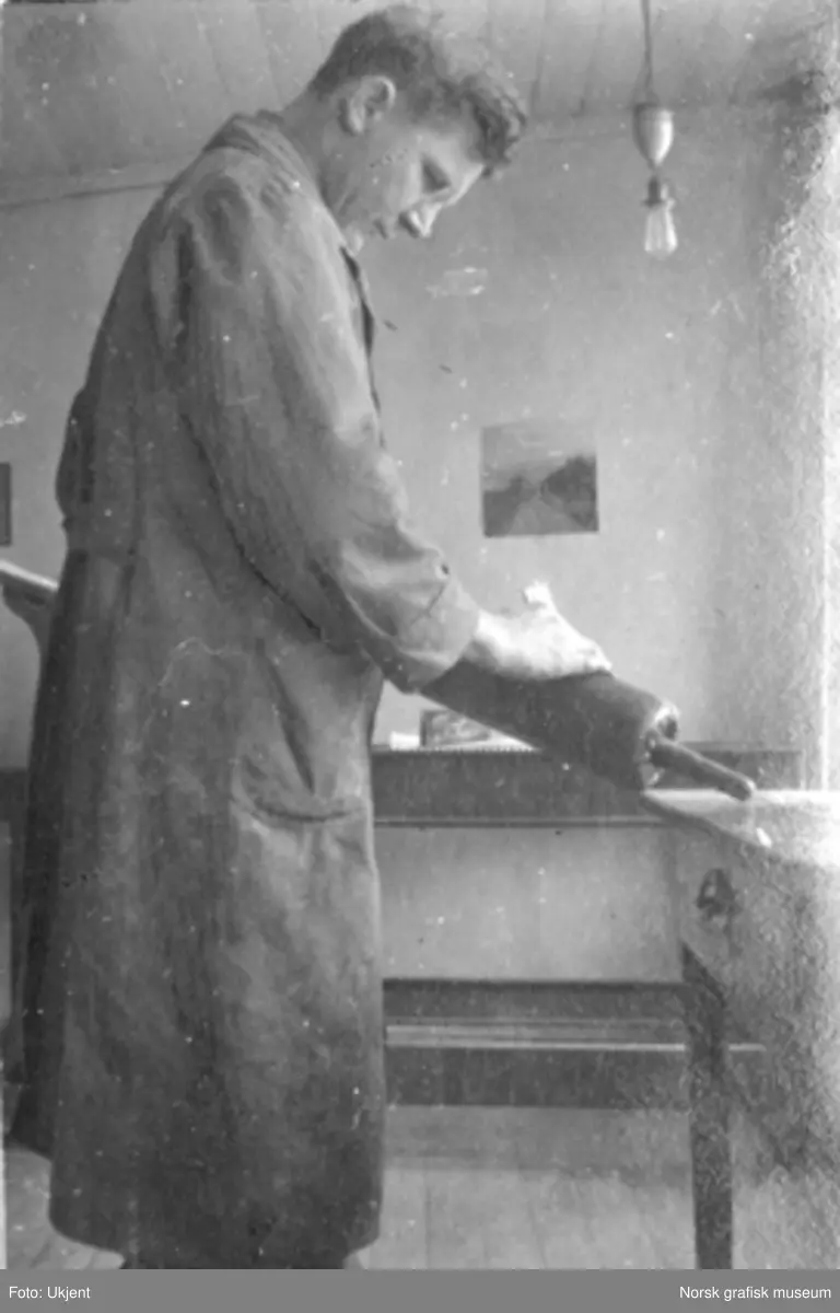 En mann i arbeidsfrakk står og rengjør en valse for trykkfarge. Innendørs på Dreyers Reproduktionsanstalt i Stavanger. Tekst under bildet i albumet: "Fra Valseverket (ikke staalverket)"