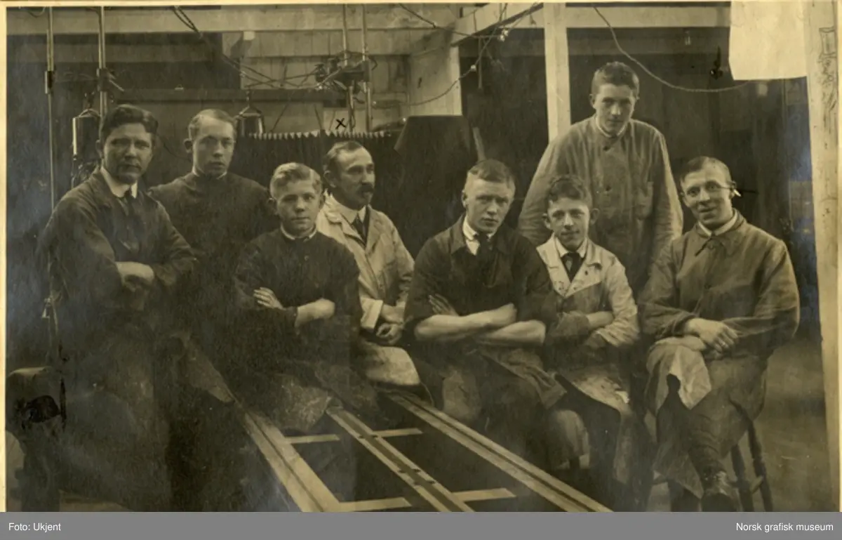 Åtte menn i arbeidstøy samlet i fotoatelieret på Dreyers Reproduktionanstalt. F.v. Gunnar Wareberg, Jakob Roalsvig, Olaf (etternavn ukjent), (fornavn ukjent) Jørgensen, (fornavn ukjent) Pettersen, Ivar Vik, Tryge Berge og Kurt Allendorf. 
Albumtekst: "Gaseren!" + navn på de avbildede. Det er også satt korstegn på avdøde.