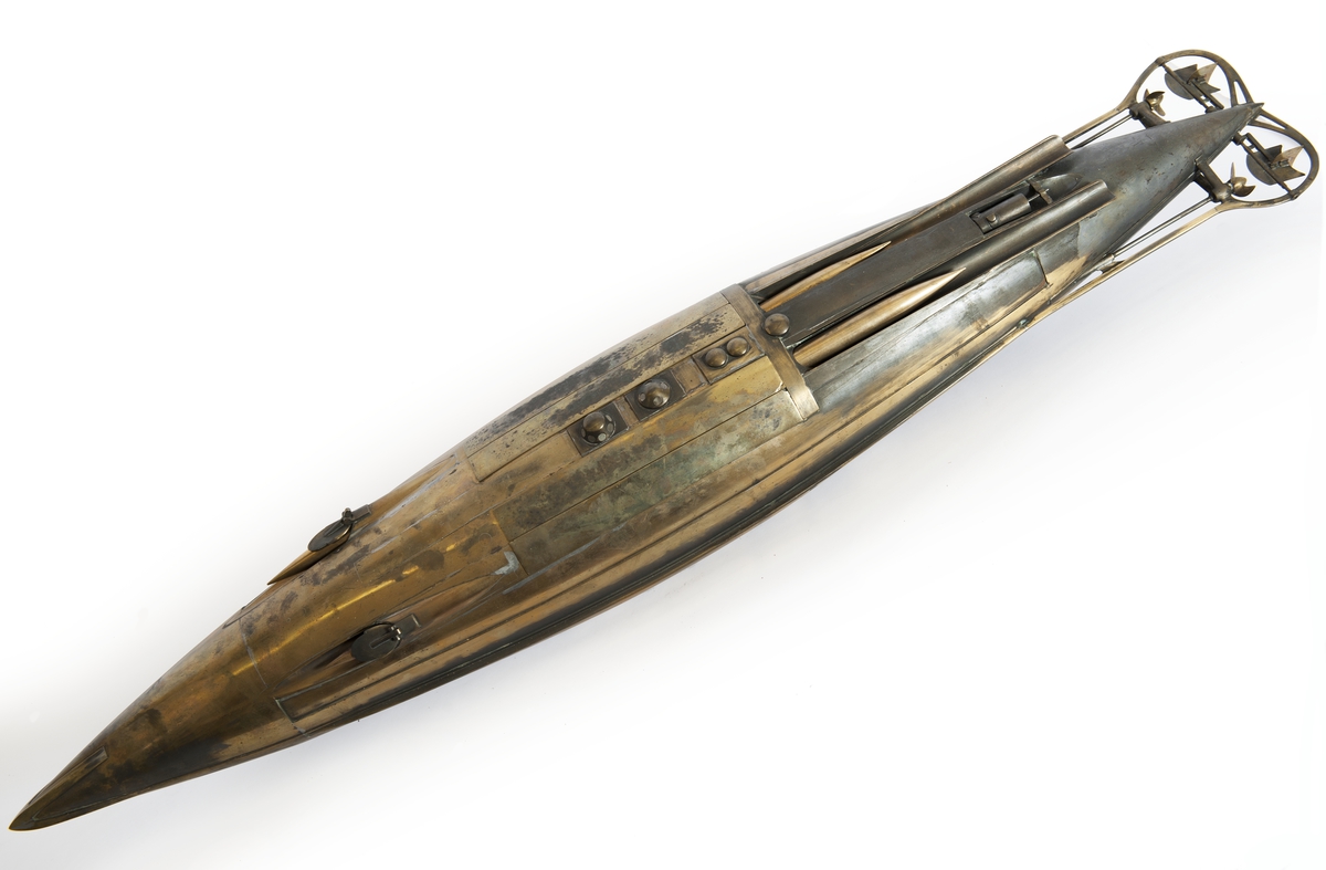 Spolformad. Stålplåt. Slingerköl, 2 propellrar av metall, 2 st höjd- och sidoroder parallellkopplade med gardjärn. 2 st höj- och sänkbara periskop av mässing. 4 st rännor för torpeder, därav 2 med luckor framtill, dels 2 för magasinering. Kort cylinder, rörlig i ränna midskepps akterut. Torpedrännorna täckas av långa stållock. Tillhörande 4 st torpeder av massiv mässing. Eneroths förslag till ubåt 1897. UndervattenstorpedFöremålets form: Spolformad.