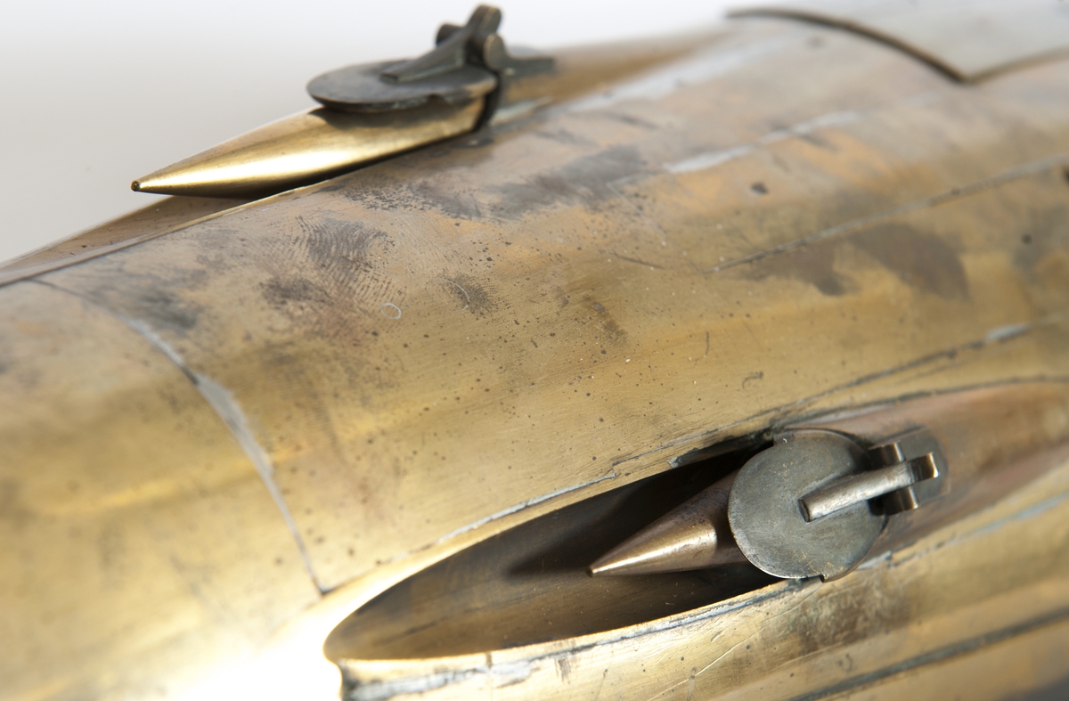 Spolformad. Stålplåt. Slingerköl, 2 propellrar av metall, 2 st höjd- och sidoroder parallellkopplade med gardjärn. 2 st höj- och sänkbara periskop av mässing. 4 st rännor för torpeder, därav 2 med luckor framtill, dels 2 för magasinering. Kort cylinder, rörlig i ränna midskepps akterut. Torpedrännorna täckas av långa stållock. Tillhörande 4 st torpeder av massiv mässing. Eneroths förslag till ubåt 1897. UndervattenstorpedFöremålets form: Spolformad.