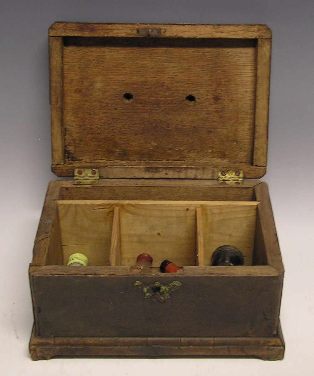 Rektangulær skrin med lokk og nøkkelhull. Liten nøkkel ligger i hullet.  Fotliste. Rommet er inndelt og inneholder små medisinflasker, krem og hodetabletter.
Ligner liten skipskiste.