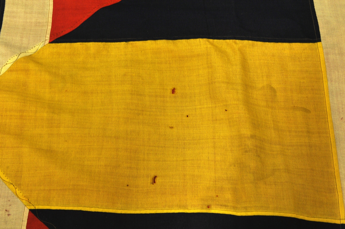 Norsk flagg med unionsmerke ("sildesalat). Unionsmerket er applikert på en rød rute øverst i høyre hjørne.
Det er påmontert  kanalgang(5,5cm) for feste av tau. Inne i kanalgangen er det antakeligvis tau av hamp. I enden av kanalgangen er det montert på en festeanordning av metall.