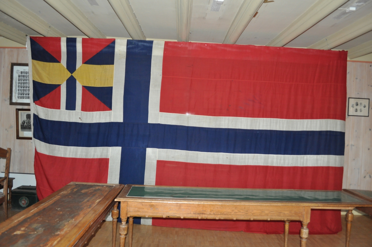 Norsk flagg med unionsmerke ("sildesalat). Unionsmerket er applikert på en rød rute øverst i høyre hjørne.
Det er påmontert  kanalgang(5,5cm) for feste av tau. Inne i kanalgangen er det antakeligvis tau av hamp. I enden av kanalgangen er det montert på en festeanordning av metall.
