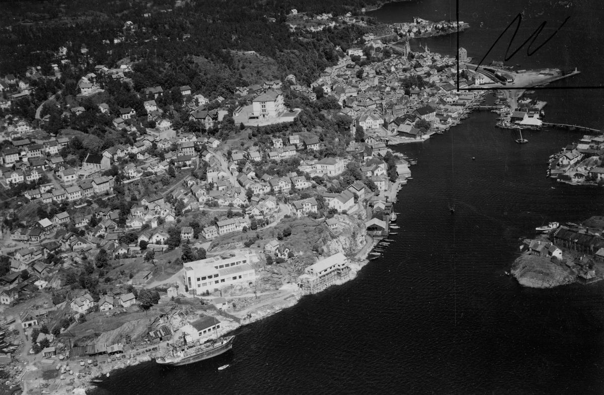 Kragerø 18/6-49. Naper og Eikeland møbelfabrikk i forgrunnen, Kragerø Folkeskole. Brua til Øya i høyre bildekant. Barthebrygga og området mot Thomesheia.