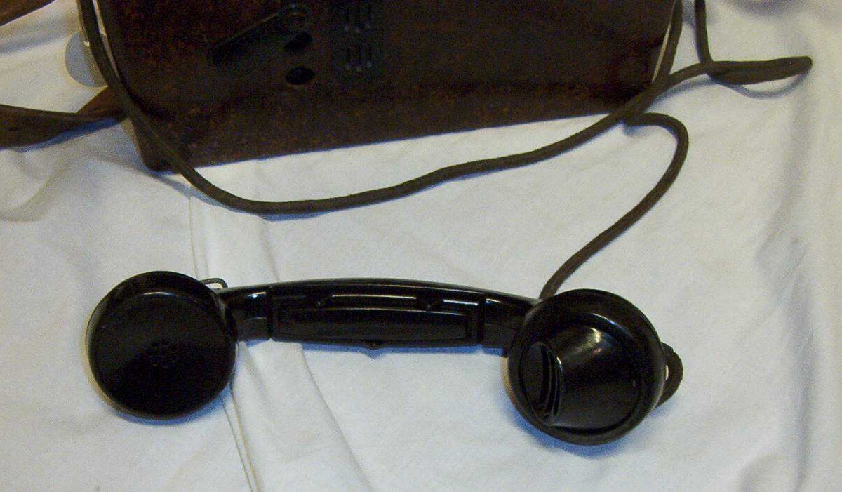 Felttelefon. Feldfernsprecher 33, FF33, tyskprodusert. Serienummer 74058.  Produksjonsår 1941. Telefonen er innebygd i bakelittkasse med bæresele. Hvit kodelapp montert på lokket. Det tyske alfabet står skrevet på lokket.