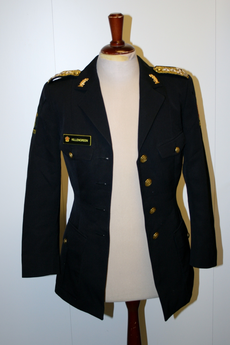 Foret, sort jakke med gullforgylte eikeløvsnåler på kraven. 4 gullforgylte knapper med riksvåpen i front og to ved splitten bak. Epåletter i flettet gull med fire stjerner og eikeløv (politidirektør). Fire lommer med klaff og knapp. Politimerke med riksvåpen på overarmene. Navneskilt i sort plast med gul skrift og riksvåpen. To ekstra navneskilt medfølger.

Knelangt, sort skjørt med glidlås bak.

Et kryssbandolær med gullforgylt rektangulær spenne dekorert med riksvåpen.

Et bredt lærbelte med gullforgylt rektangulær spenne dekorert med riksvåpen.

Et smalt lærbelte med gullforgylt rektangulær spenne dekorert med riksvåpen.

Politilue med hvit pull og luemerke i gull og rødt og eikeløvsbroderier i sort og gull. To forgylte knapper holder luesnoren på plass. (Lue for vinterhalvåret (med sort pull) registrert på NRM.03690)

Slips, skjorte og hvite hansker medfølger ikke.