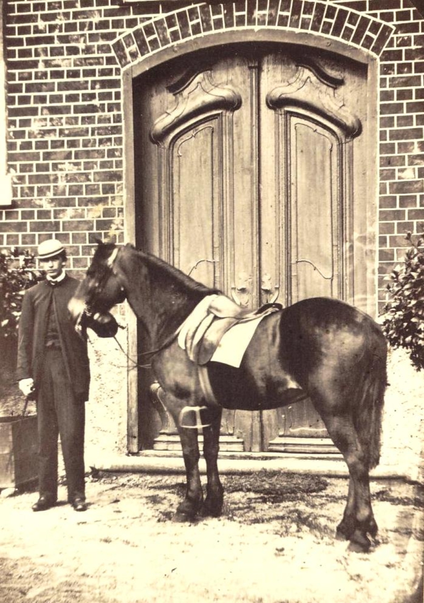 Foto av Fredrik Faye stående med ridehest foran inngangsdør i 1863
