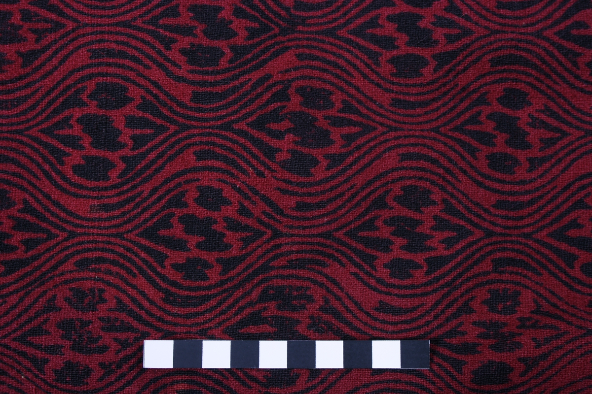 Ulveskinnspels, Lang og noe utskrådd. 
Sydd sammen av mange smale pelsstykker, to i høyden. En liten splitt midt bak. Ermer sydd sammen av mindre pelsstykker. Ermene har en liten oppbrettet fald av pelsen i nedkant, på resten av plagget er pels og fór sydd sammen kant i kant, ute belegg eller oppbrettet fald. Sjalskrage med underkrage av sort kunstpels. Underkragen har søm midt bak. 
Fóret med rødt klede med sort trykk, også i ermene.
Hele plagget er håndsydd med grov tråd, selve pelsen med ubleket lintråd. Fóret er sydd sammen, og sydd til pelsen, med ubleket eller sort bomullstråd. Fóret har sidesømmer, men ingen søm i ryggen. Ryggstykket er kvadratisk med trådrette sider. Forstykkene er trådrette midt foran og skrådd i siden. I sidene er det satt inn en liten kile nederst. 
I nedkant av kragen i venstre side er det en stor sølvhekte, gravert med blomstermotiv. Ingen tegn til annen lukning.  
Stor lærhempe i nakken.