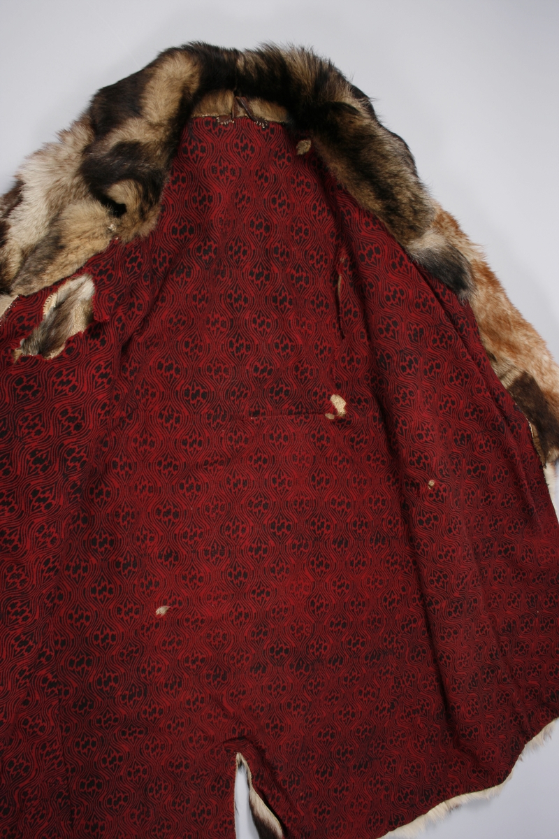 Ulveskinnspels, Lang og noe utskrådd. 
Sydd sammen av mange smale pelsstykker, to i høyden. En liten splitt midt bak. Ermer sydd sammen av mindre pelsstykker. Ermene har en liten oppbrettet fald av pelsen i nedkant, på resten av plagget er pels og fór sydd sammen kant i kant, ute belegg eller oppbrettet fald. Sjalskrage med underkrage av sort kunstpels. Underkragen har søm midt bak. 
Fóret med rødt klede med sort trykk, også i ermene.
Hele plagget er håndsydd med grov tråd, selve pelsen med ubleket lintråd. Fóret er sydd sammen, og sydd til pelsen, med ubleket eller sort bomullstråd. Fóret har sidesømmer, men ingen søm i ryggen. Ryggstykket er kvadratisk med trådrette sider. Forstykkene er trådrette midt foran og skrådd i siden. I sidene er det satt inn en liten kile nederst. 
I nedkant av kragen i venstre side er det en stor sølvhekte, gravert med blomstermotiv. Ingen tegn til annen lukning.  
Stor lærhempe i nakken.