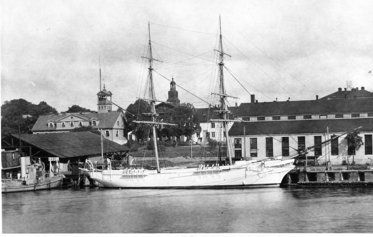 Bilden visar skeppsgossefartygen övningsbrigg Falken förtöjt vid kajen framför den numera rivna tackelkammaren i Karlskronas örlogshamn.