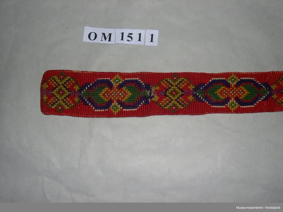 Eit par mannsseler brodert med halve krossting. Hovudfarge er raud, med mønsterdekor i lilla, grønt og gult. Her er òg felt som ikkje er sydd slik at den ubleika strameifargen under kjem fram. Selane har hemper på baksida til festing på buksa. Litt slitt.