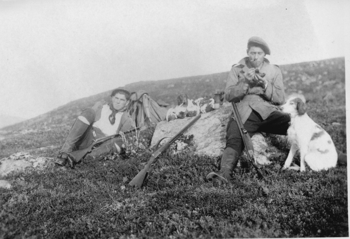 To menn på jakt i fjellet. Ryper på en stein i midten, og hund til høyre.