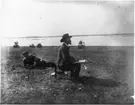 'Intendent Olof Gylling, sittande, och Leonard Axel Jägerskiöld, liggande, vid Hornborgasjön. Olof Gylling målar. ::  :: Olof Gylling besökte Hornborgasjön tillsammans med Leonard Axel Jägerskiöld under år 1919 i syfte att välja ut motiv för diorama. Detta enligt Göteborgs Naturhistoriska Museums Årstryck 1920.'