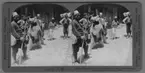 'Uppvisning med björn gående på bakbenen. 7 män och pojkarkring björnen. ::  :: '' 10966 - Turkish Venders and entertainers, Adana, Asiatic Turkey, center of massacres, April, 1909.''. ::  :: Ingår i serie med fotonr. 315-422.'