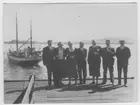 'Gruppbild från Biologiska Stationen i Trondheim, på brygga, vy ut mot havet. :: Fr.v. Dr Nils Odhner, fröken Fröseth, fru Hanson, Fru Hansons nevö, professor Leonard Axel Jägerskiöld, Sune Swärd och Kapten Hanson. I bakgrunden syns båten ''Gunnersro''. :: Även fotonr 3692. ::  :: Ingår i serie med fotonr. 3694-3719 se även fotonr. 3679-3693.'
