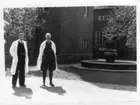 'Dr Orvar Nybelin och amanuens Paul Henrici på museigården. ::  :: Stående i vita rockar i solsken med ryggen mot ingången till museet. Springbrunnen, fontänen, med 3 pingviner synlig, gjord av Sigrid Friman.'