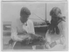 'Orvar Nybelin (till vänster med pipa i munnen) flaskmatar en knubbsälunge tillsammans med 1 flicka som sitter till höger med glasflaska med napp. I bakgrunden stor båt. ::  :: Se även fotonr. 481.'