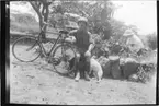 'Diverse fotografier från bl.a. dåvarande Nordrhodesia, nu Zambia, tagna av Konsul Magnus Leijer. ::  :: En man sittandes, på en låg stenmur, m en cykel och en hund. I en blomsterplantering bakom honom leker ett barn.'