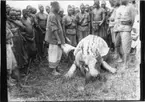 'Diverse fotografier från bl.a. dåvarande Nordrhodesia, nu Zambia, tagna av Konsul Magnus Leijer. ::  :: En till hälften flådd flodhäst liggande på mage i mitten av en cirkel av män, bredvid kroppen står också en man med en kniv i handen.'