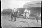 'Diverse fotografier från bl.a. dåvarande Nordrhodesia, nu Zambia, tagna av Konsul Magnus Leijer. ::  :: 1 st kvinna och 1 st man sittande på varsin häst. 1 st man stående bredvid, på en veranda bakom dem står 1 st flicka.'