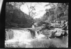 'Diverse fotografier från bl.a. dåvarande Nordrhodesia, nu Zambia, tagna av Konsul Magnus Leijer. ::  :: Klippor i forsande vatten, på de olika avsatserna står människor, fotograferade från avstånd.'