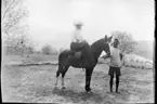 'Diverse fotografier från bl.a. dåvarande Nordrhodesia, nu Zambia, tagna av Konsul Magnus Leijer. ::  :: 1 st man håller i en hästs tyglar, på hästen sitter 1 st kvinna. Bakom den öppna plats de står på vatten synligt.'