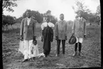 'Diverse fotografier från bl.a. dåvarande Nordrhodesia, nu Zambia, tagna av Konsul Magnus Leijer. ::  :: Tre män, en kvinna och ett barn, stående på en öppen gräsplats, bakomdem är träd och staket synligt. Barnet står tätt mot en av männens ben.'