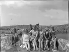 'Gruppbild med badklädda kvinnor, barn, flickor, pojkar. Gruppen iklädda badkläder och sittande på berghäll vid havet. ::  :: Ingår i serie med fotonr. 5236:1-11.'