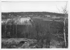 'Bildtext: ''Sedimentyta. Hällar. Riktning 88.'' I förgrunden berghällar med bl.a. björkvegetation, sluttning ner mot sedimentytan med öppna fält, åkrar. På avstånd hus, gårdsbyggnader och i bakgrunden berghällar med skog. ::  :: Ingår i serie med fotonr. 6970:1-1125, dokumentation av Hisingens naturgeografi, visande landskapsformerna i stora drag och gjord inför exploateringen av området. Platserna för fotograferingen finns utsatta på karta i skala 1:4000 som finns på Göteborgs Naturhistoriska musem. Fotoriktningen mättes med kompass i gammalgrader.'